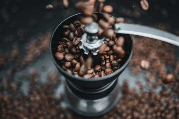 Roasted coffee beans in the grinder Fried coffee beans are falling to the manual grinder. Cinematic dark  colors. Preparation of fresh beverage morning coffee for breakfast. Mill for grinding. Isolated on black background. slow motion stock pictures, royalty-free photos & images