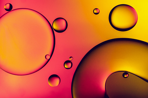 Colourful patterns of oil drops in water against vibrant defocused background extreme close-up
