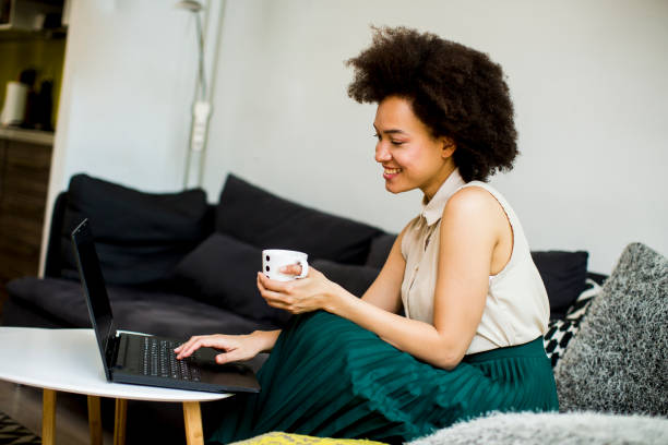 istock Young beautiful lady with curly hair work on the notebook while sit down on the couch at home 1219192448