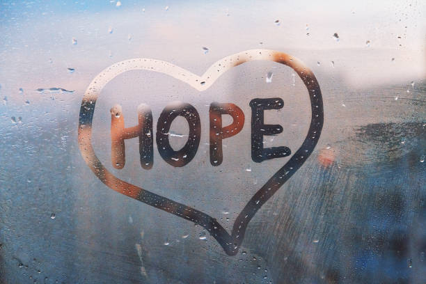 Foggy glass on window with written finger word yellow color Hope in paint heart concept photo with copy space on blue and warm background Handwritten word Hope in shape heart on misted glass on window flooded with raindrops on blue cloudy background single word stock pictures, royalty-free photos & images