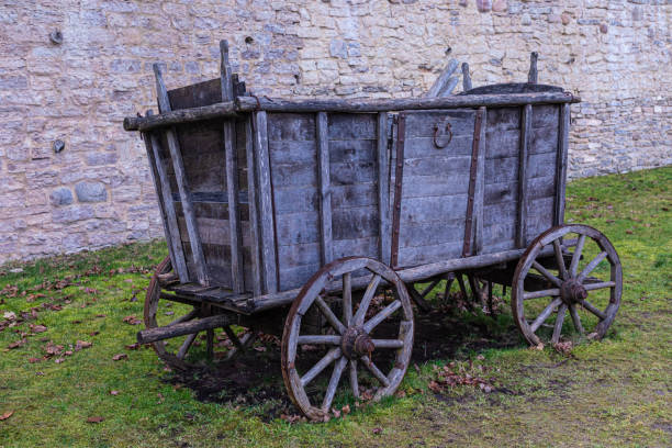 22 Feb 2020. Pskov, Russia. The broken ancient medieval rural wood cart or wagon on the green grass on the background of the castle or fortress stone or brick wall