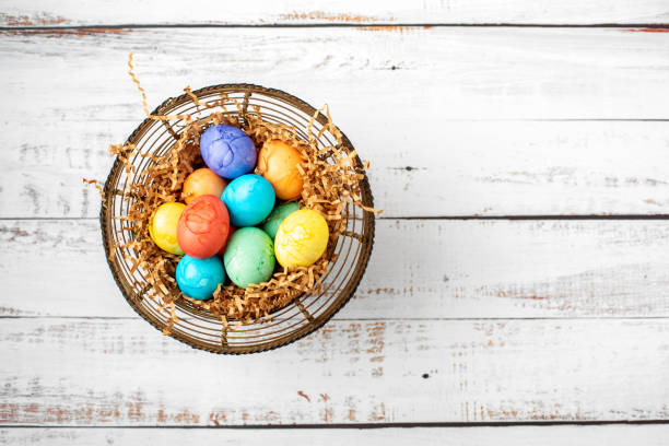 istock Brightly Colored Easter Eggs in a Wire Basket on a White Wood Table 1219203279