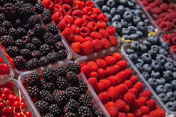 many plastic containers with berries: raspberries, blueberries, blackberries for sale.