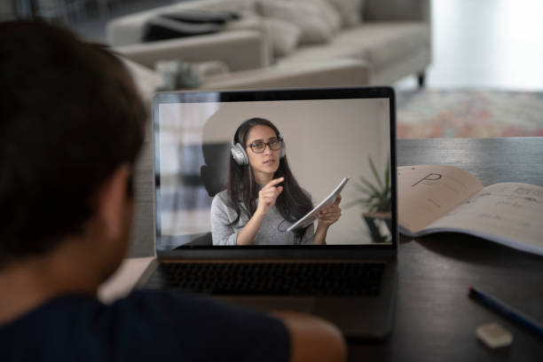 Male student learning online from remote teacher Young male student listening and participating in online class lesson at home from a teacher, in order to social distance, quarantine, and learn from home. online tutors stock pictures, royalty-free photos & images