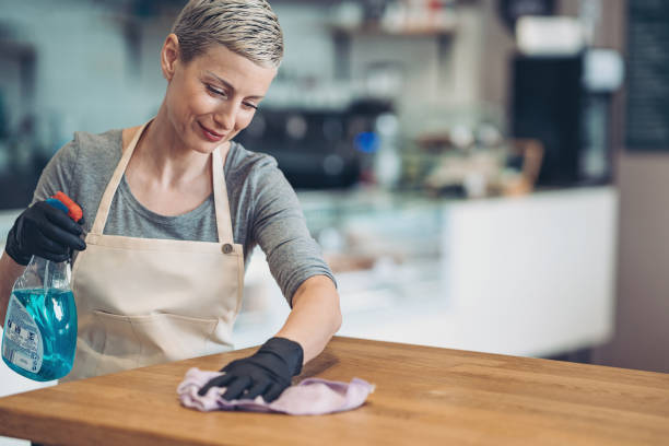 Young woman carefully cleaning a table with a sanitizing spray Waitress cleaning a table housekeeping staff photos stock pictures, royalty-free photos & images