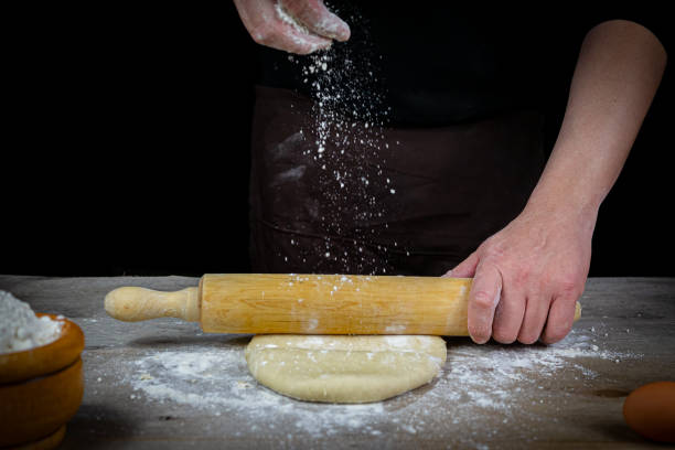 istock Man hands kneading bread dough on a wooden table with black background 1219207877
