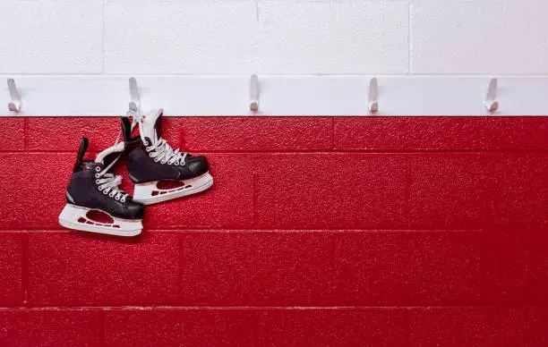 Photo of Hockey skates hanging over red wall in locker room with copy space