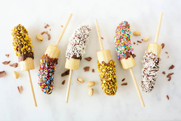 istock Frozen chocolate dipped banana pops, top view scattered on white marble 1219210148