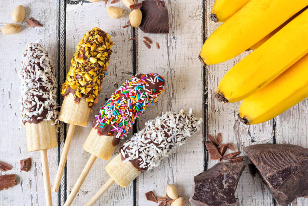 istock Frozen chocolate dipped banana pops, above view table scene over rustic white wood 1219210244