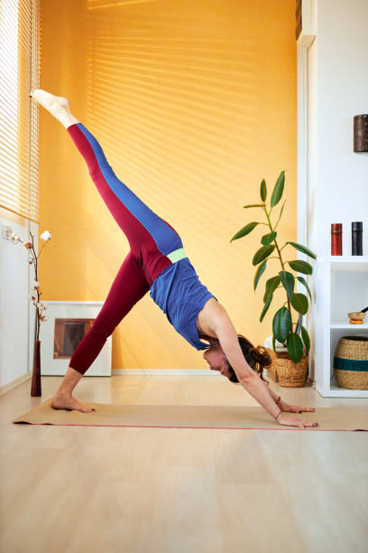 istock Attractive fit Caucasian middle aged brunette doing Three Legged Downward-Facing Dog yoga pose in the morning. Home interior. 1219211087