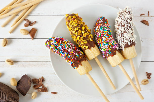 istock Frozen chocolate dipped banana pops, overhead view table scene on a wood background 1219211294