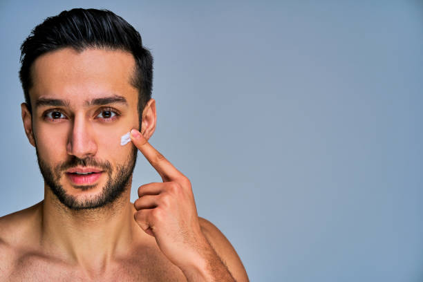 istock Closeup guy with beard with a smile applying white cream on his cheek by finger. Cosmetics concept 1219211766