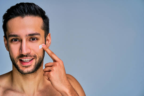istock Closeup guy with beard with a smile applying white cream on his cheek by finger. Cosmetics concept 1219211785