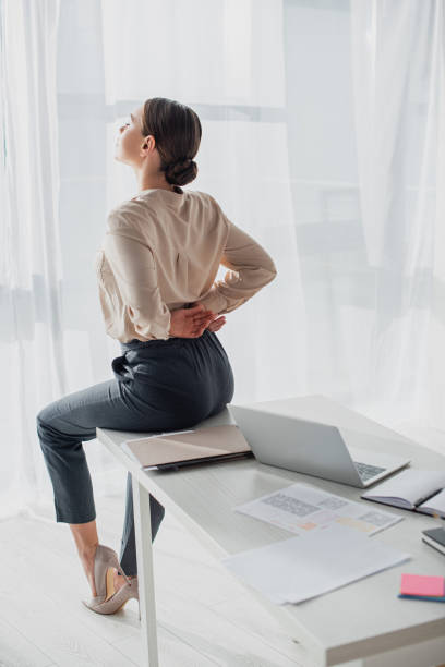 istock tired businesswoman stretching back on workplace with laptop 1219214345