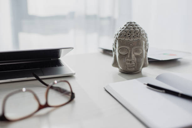 istock Buddha head, eyeglasses, notepad and laptop on table at workspace 1219214351
