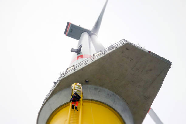 Manual high worker offshore climbing on wind-turbine on ladder in north sea. stock photo