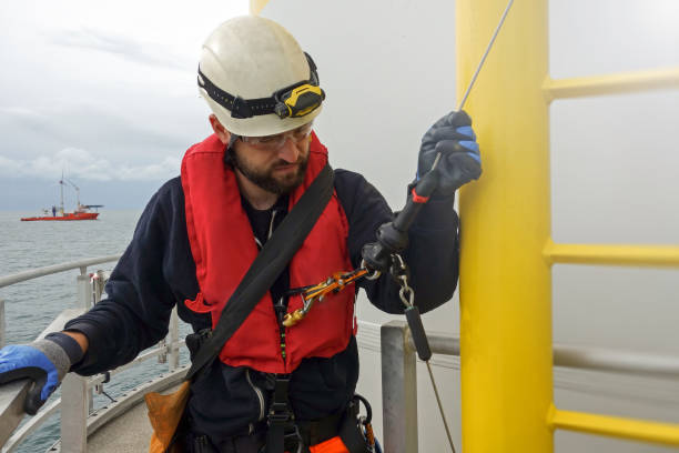 istock Rope access technician is preparing for climbing down from wind turbine - offshore platform. Big transfer vessel is behind. 1219217202