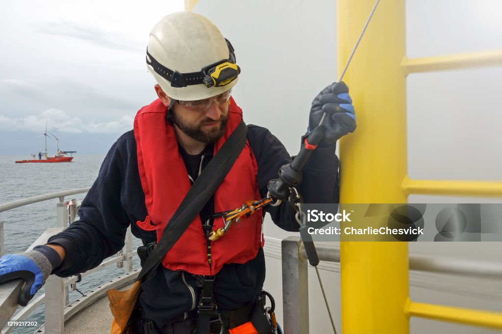 Rope access technician is preparing for climbing down from wind turbine - offshore platform. Big transfer vessel is behind. Sea Stock Photo Rope access technician is preparing for climbing down from wind turbine - offshore platform. Big transfer vessel is behind. Sea Stock Photo