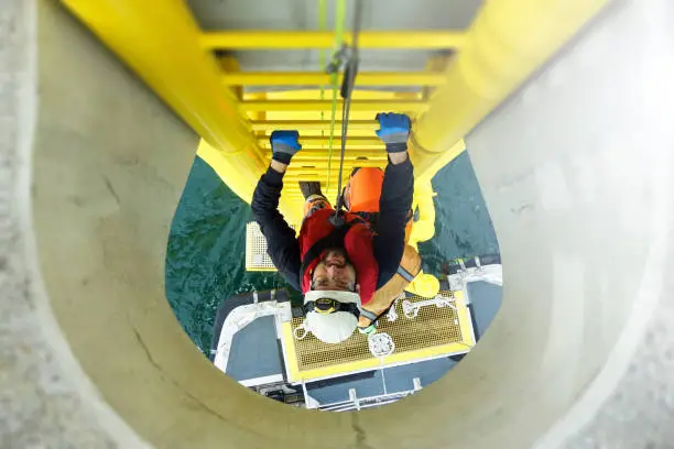 Manual high worker offshore climbing on wind-turbine on ladder and transfer vessel waiting under wind turbine