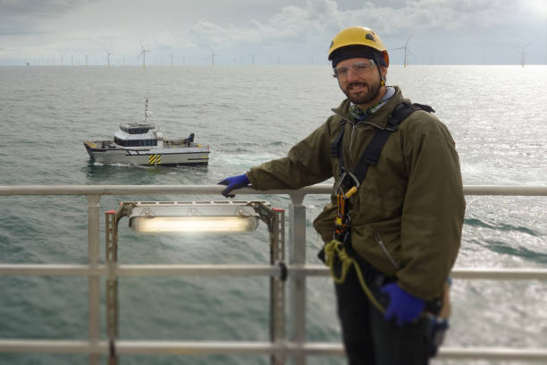 istock Smiling Technician waiting for transfer vessel on offshore platform - wind turbine and looking in camera. Offshore Wind farm is behind. 1219217226