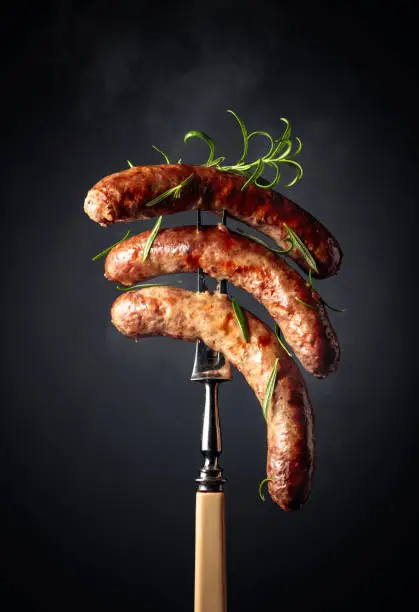 Grilled Bavarian sausages with rosemary. Sausages on a fork sprinkled with rosemary.