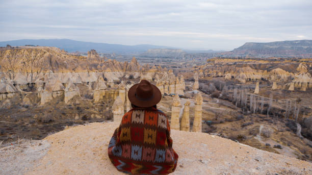Woman alone watching mushroom shaped fairy chimneys at love valley in Cappadocia, Turkey. Woman watching the volcanic landscape at the valley of love in Goreme, Cappadocia cappadocia winter photos stock pictures, royalty-free photos & images