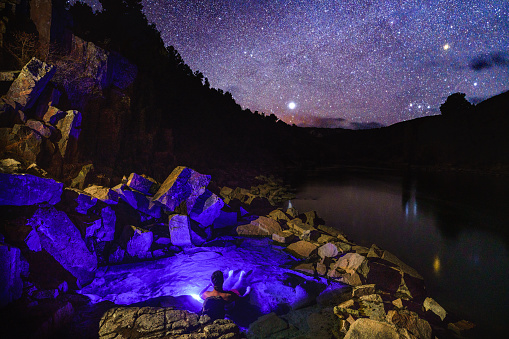 Man Soaking in Outdoor Natural Hot Springs Under the Stars - Night scenic view of stars and man soaking in natural hot spring along scenic river with very dark skies.