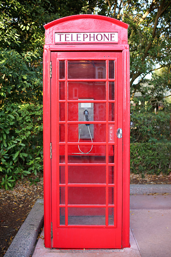 An old fashioned British style red painted telephone booth box sits on a sidewalk.