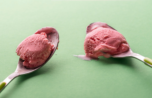 Two spoons of raspberry ice cream on a green background. Close-up of fruity ice cream eaten with spoons. Delicious summer refreshing dessert.