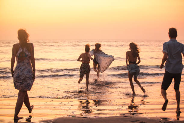 A wide shot of a group of friends running into the sea at Kuta beach in Bali, Indonesia at dusk.