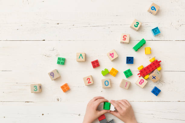 vista superior en las manos de los niños jugando con cubos de madera con números y coloridos ladrillos de juguete sobre fondo de madera blanca. bebé con juguetes - cube baby child block fotografías e imágenes de stock