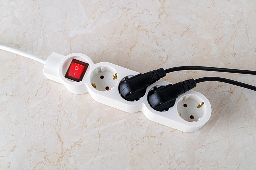 Power button on a white extension cord with four outlets. Electric power strip with switch for home or office. Household appliances. Top view.