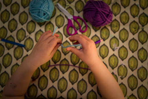 View from above: Hands of a little girl getting creative  at home during coved-19 coronavirus pandemic with lockdown homeschooling requirement. Shot indoors and with lens flare