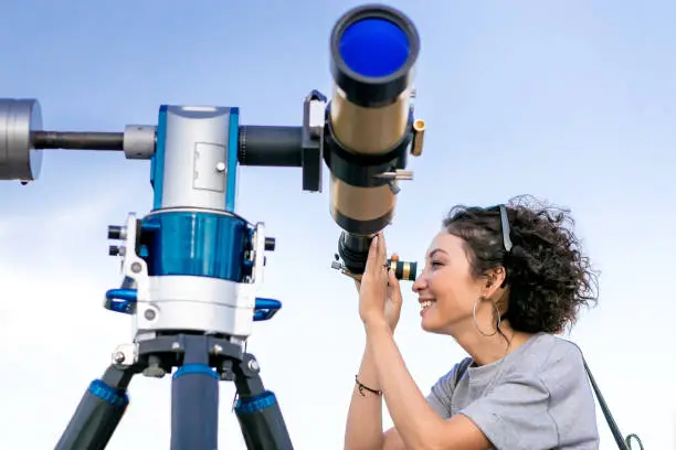 Young smiling woman looking skyward through astronomical telescope
