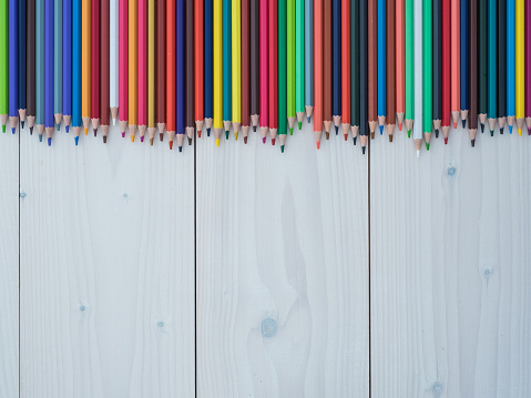 Set of colored pencils arranged in a row on wooden background. top view
