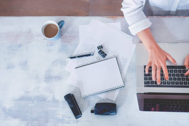 istock Top view of woman using laptop while sitting at the table with laptop, mobile phone, note pad, coffee cup. 1219256269