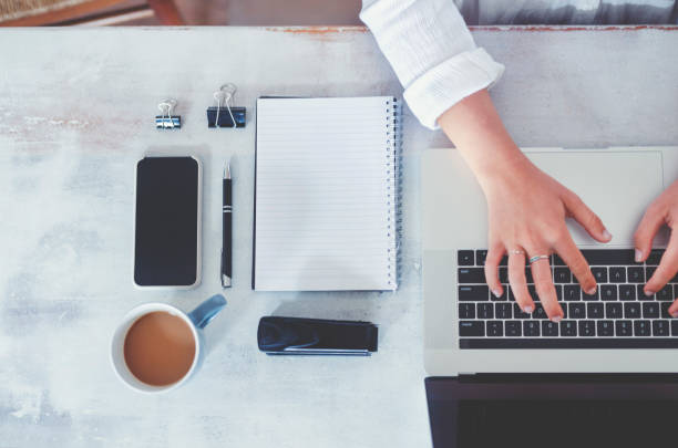 istock Top view of woman using laptop while sitting at the table with laptop, mobile phone, blank note pad and pen. 1219256273