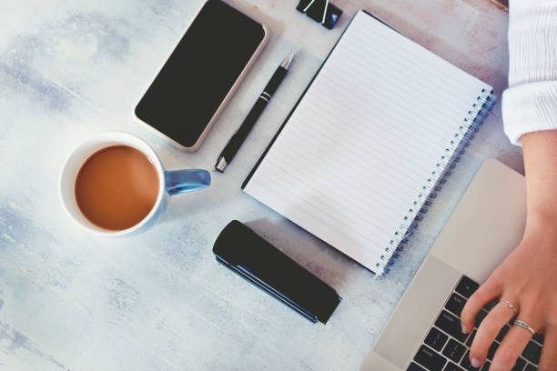 istock Top view of woman using laptop while sitting at the table with laptop, mobile phone, blank note pad and pen. 1219256274