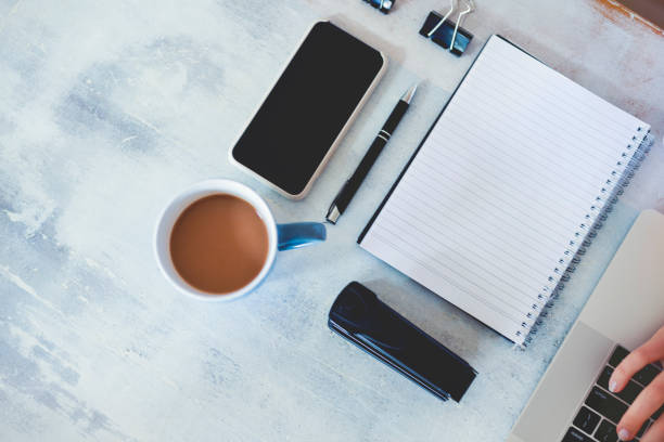 istock Top view of woman using laptop while sitting at the table with laptop, mobile phone, blank note pad and pen. 1219256275