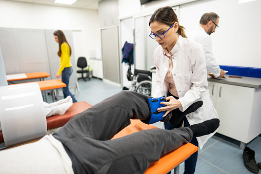 A young female doctor prepares a patient for leg exercises with weights.