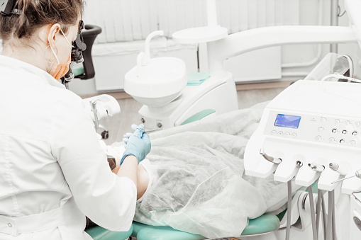 careful professional dentist in white uniform treating patient's teeth, making perfect smile for patients, using medical equipment
