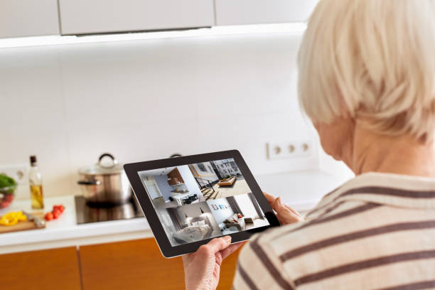 istock Retirement. Senior woman standing controlling smart home on digital tablet back view watching camera close-up 1219263786