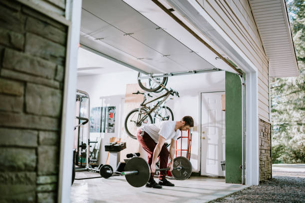 Man Doing Exercise Workout in Garage A mid adult man lifts weights in his home garage.  Part of a regular routine, or the new normal with social distancing and Covid-19. center athlete stock pictures, royalty-free photos & images