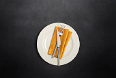 Table setting with white plate, fork and knife cutlery and linen napkin on dark table