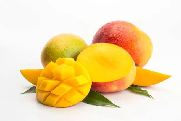 Photographic composition of mangoes on white background, two whole and one halved. One of the halves is cut into cubes. There are also some leaves of mango tree in the composition.