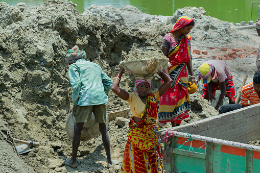 Howrah, West Bengal, India - 7th May 2017 : Indian male and female workers digging and carrying out soil at buliding construction site. India has a huge population of daily wage earners.