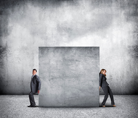 A businessman and a businesswoman work against each other as they attempt to move a large concrete block