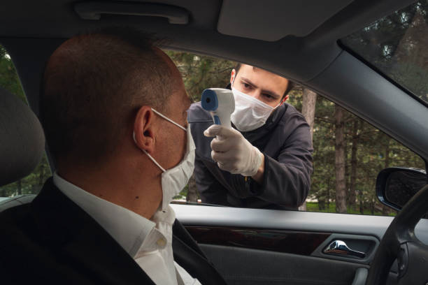 Shot of a security guy measuring a driver's body temperature with thermometer stock photo