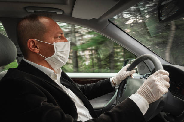 Side view of a senior adult wearing surgical mask and gloves driving his car stock photo