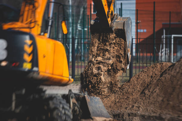 escavatore pesante giallo che scava sabbia e lavora durante i lavori stradali, scaricando sabbia durante la costruzione della nuova strada con i lavoratori intorno - archeologia foto e immagini stock